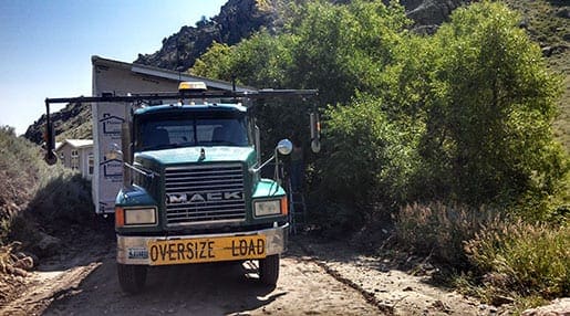 Green semi truck moving a mobile home through a narrow rural road